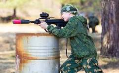 Outdoor laser tag player aiming from behind cover in an outdoor field setting