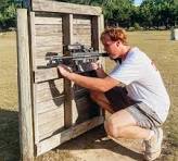 Player aiming around a wooden barricade during an outdoor laser tag match